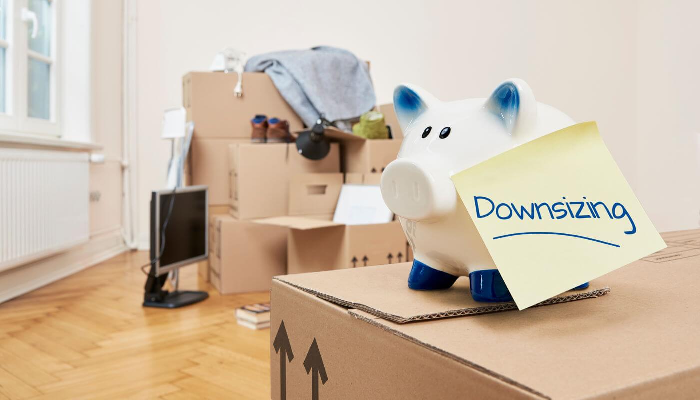 A piggy bank on top of moving boxes with a note that says downsizing.